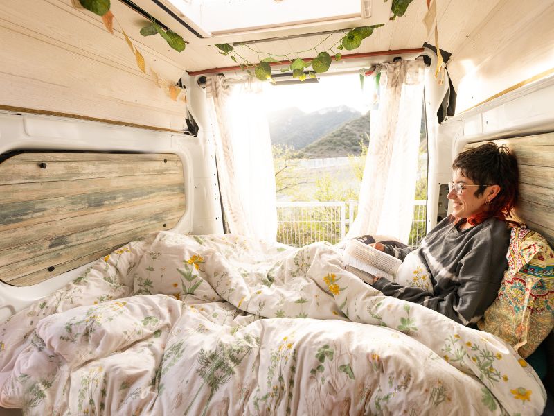 Una persona leyendo un libro sobre un colchón en una furgoneta camper.